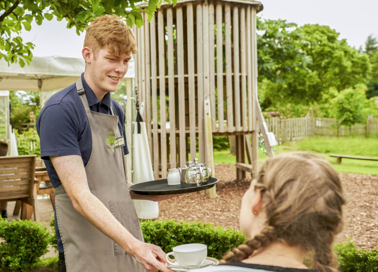 A team member serves tea to a customer outside at The Balloon Tree cafe