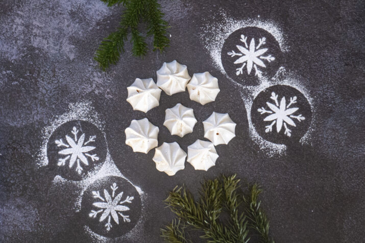 Mini Meringue Kisses surrounded by Christmas tree branches and icing sugar snowflakes